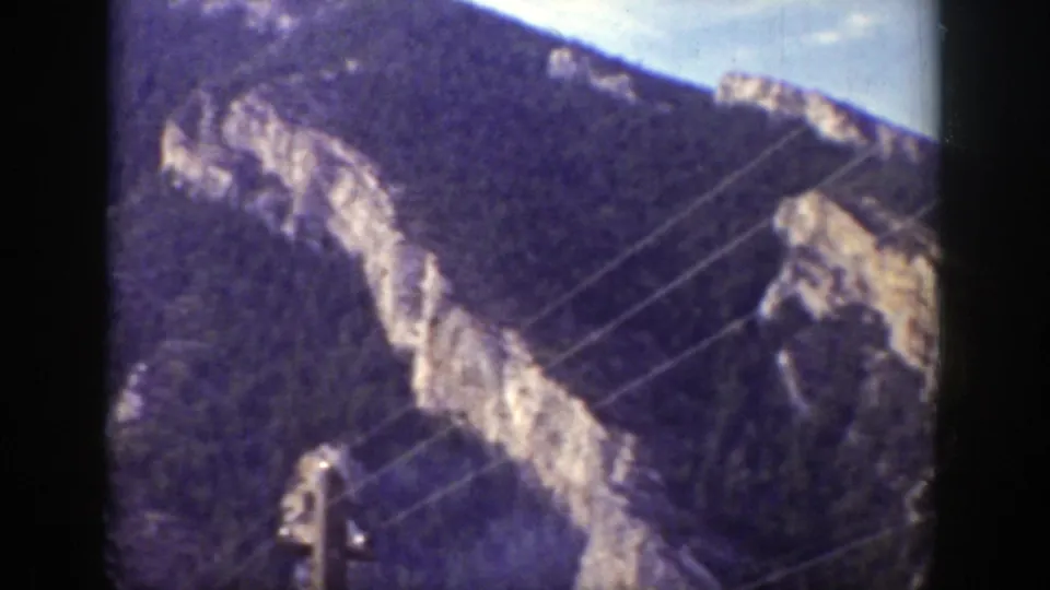 Vintage 8mm Wyoming frame showing diagonal utility wires in front of gray rock and dark mountain vegetation.