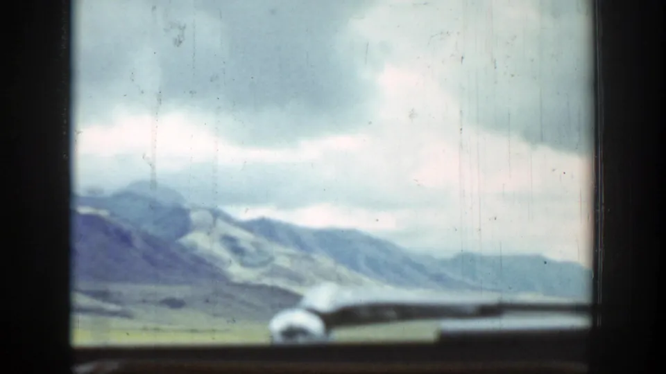 1939 Wyoming road-view frame with distant mountains, overcast sky, and a vehicle hood at the bottom edge.