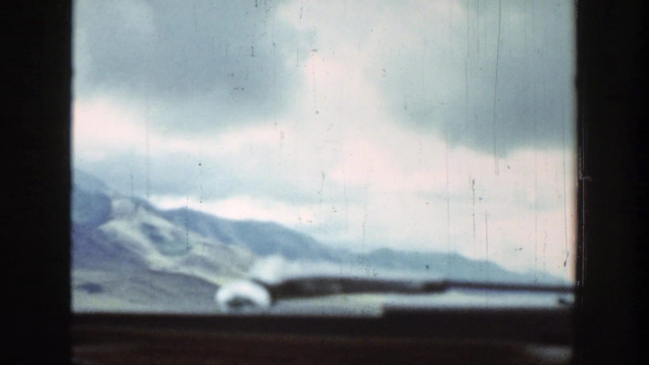1939 Wyoming 8mm car-window view showing distant mountains, green fields, and a cloudy sky through a dark vehicle frame.