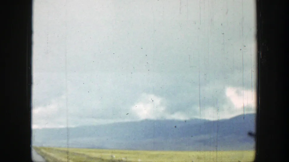 End frame of 1939 Wyoming 8mm footage with open grassland, low blue ridge, cloud cover, and a partial car-window edge.