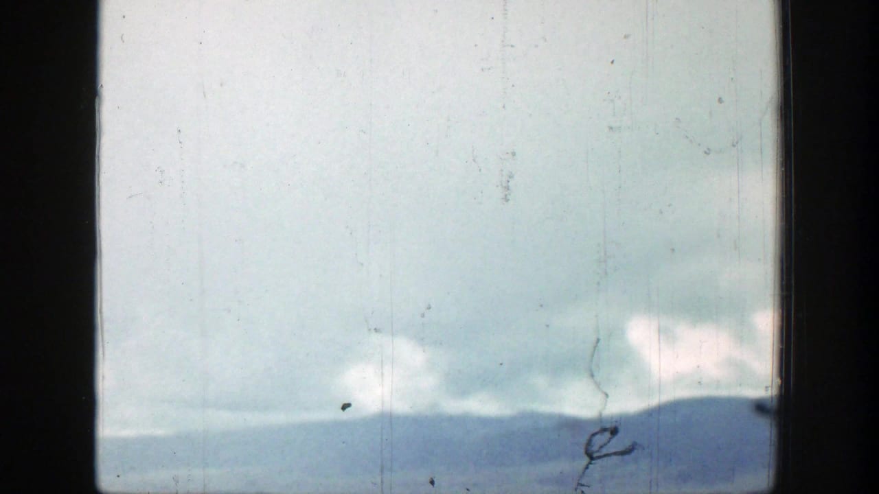 1939 Wyoming home-movie frame of a distant mountain ridge and cloudy blue sky seen through a dark window-like frame.