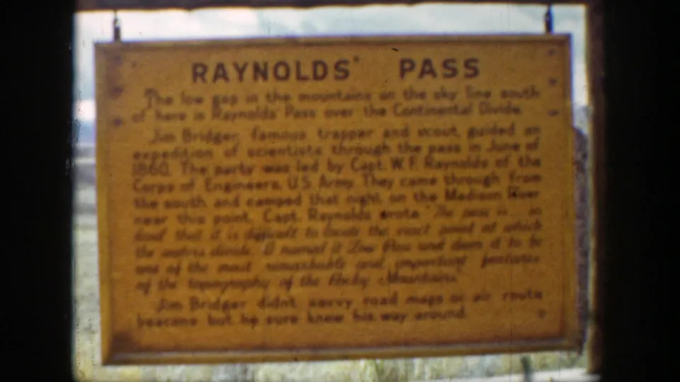 Yellow Reynolds Pass roadside sign in front of a cloudy mountain landscape, filmed in 1939 Wyoming home-movie footage.