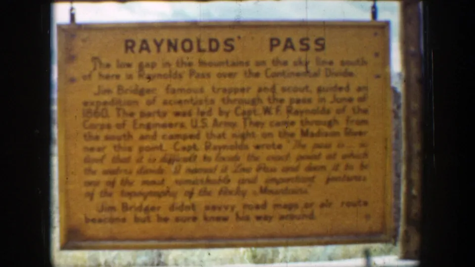 1939 home-movie frame of the Raynolds' Pass roadside marker, showing its framed board and explanatory lettering.