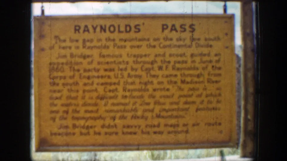Final 8mm frame of the Raynolds' Pass sign, with the outdoor marker still centered against a soft background.