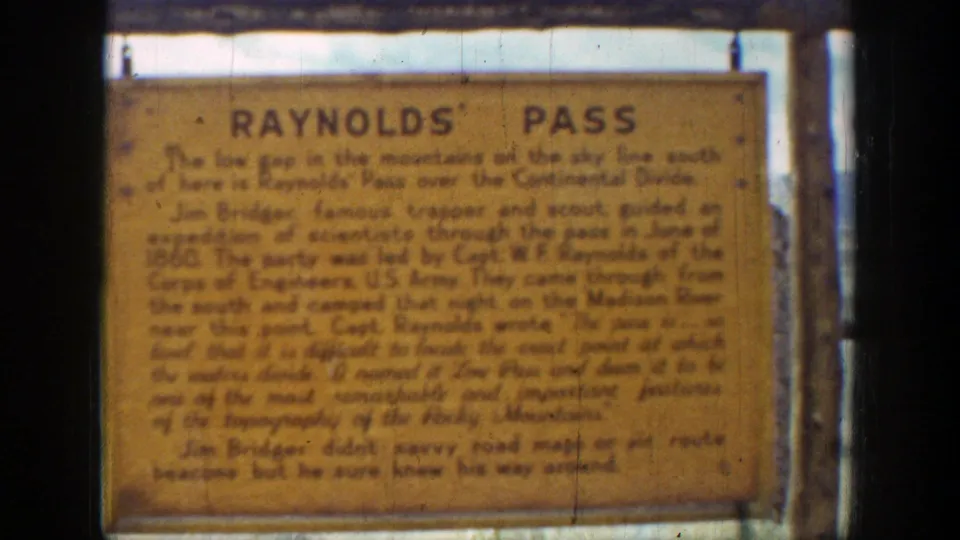 Close 8mm view of the Reynolds Pass sign in Wyoming, with legible title, soft focus, scratches, and warm faded color.