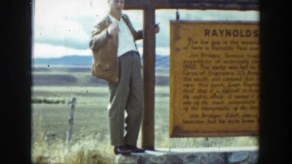 A man in a jacket and light trousers poses beside the Reynolds Pass sign in a 1939 Wyoming home-movie travel scene.