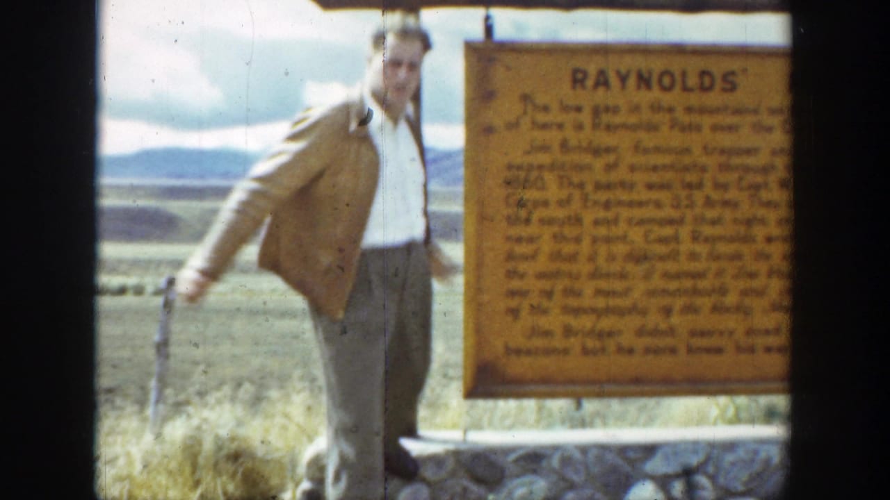 1939 Wyoming 8mm frame showing an adult man beside a Raynolds historical marker with open grassland and distant hills behind him.