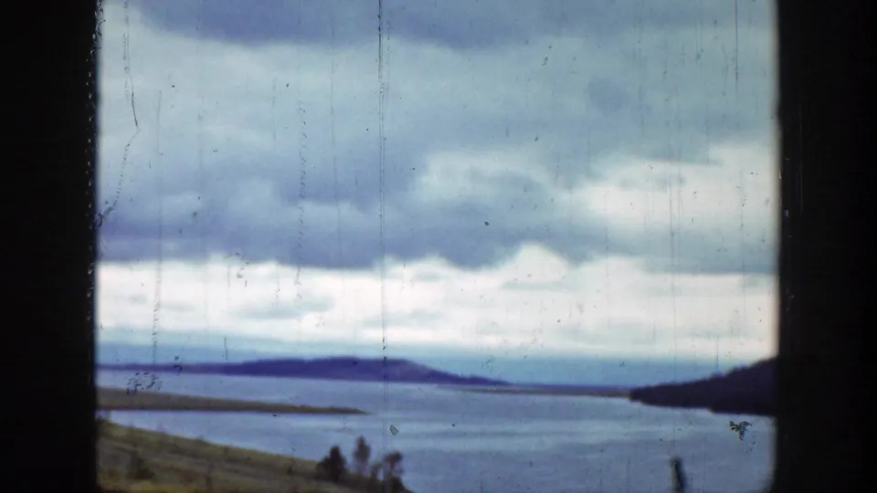 Wyoming lake or reservoir view under heavy clouds, framed by dark 8mm film borders and distant low hills.