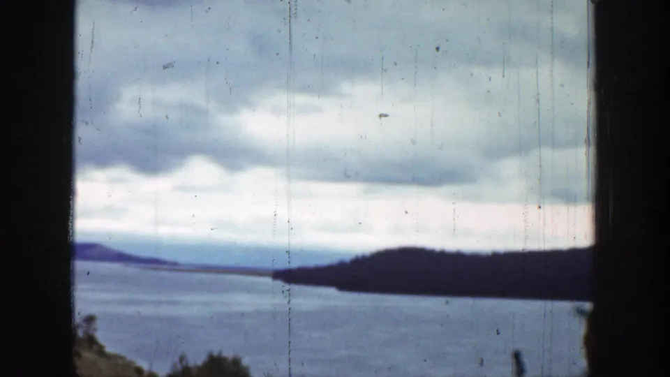 Wide 1939 Wyoming landscape frame showing a lake, wooded or dark shoreline, pale cloud cover, and vertical film wear.