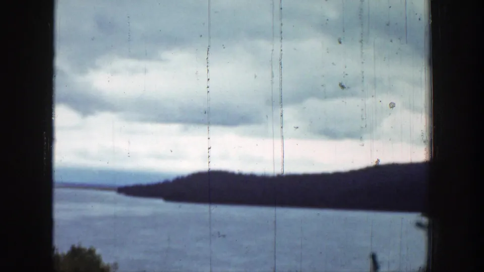 Final 8mm frame of a Wyoming lake scene, with a dark hillside across the water and cloudy sky above.
