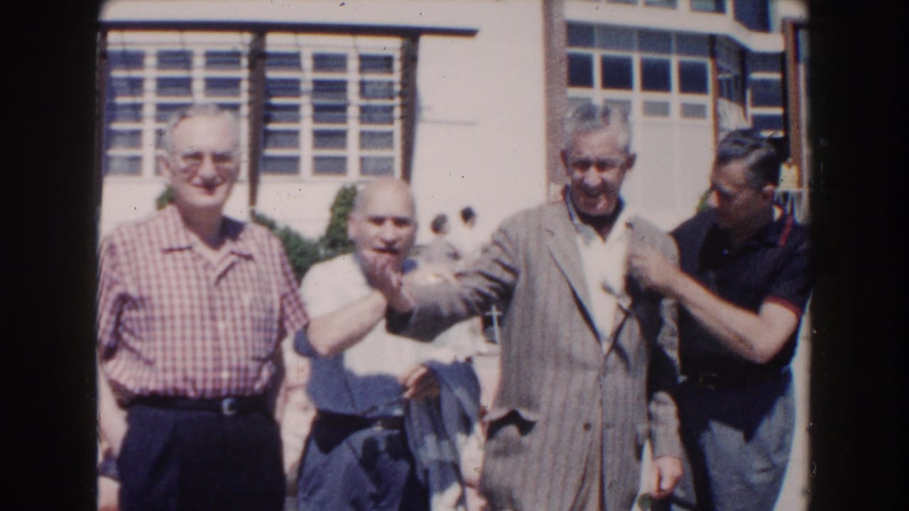 Several elderly men pose together outdoors beside a pool area.