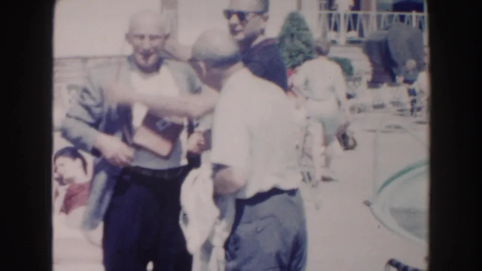Older men interact near a Miami pool area, with lounge chairs and other seated people visible behind them.