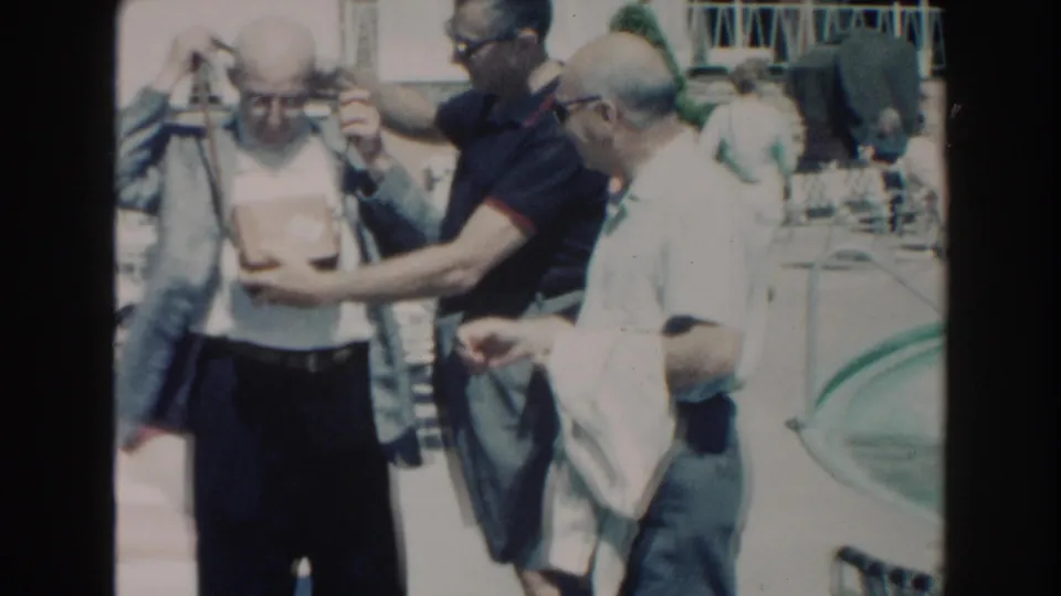 Older men in casual shirts stand close together on a Miami pool deck, with a pool and railings nearby.