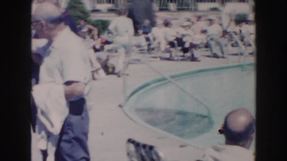 A Miami poolside scene shows an older man partly in the foreground, with swimmers or seated visitors and lounge chairs beyond.