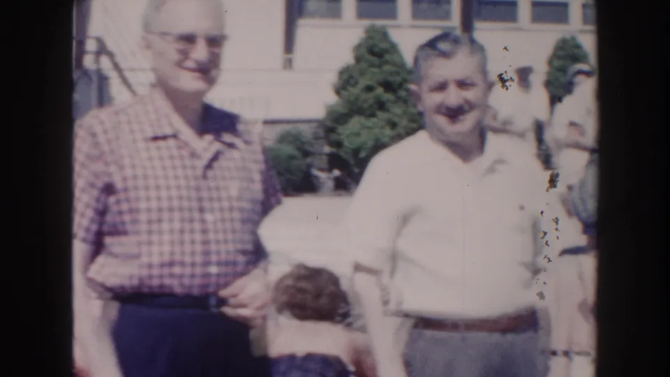 1960 Miami frame showing two adult men standing near the poolside, with a shorter partially visible figure at the bottom edge.