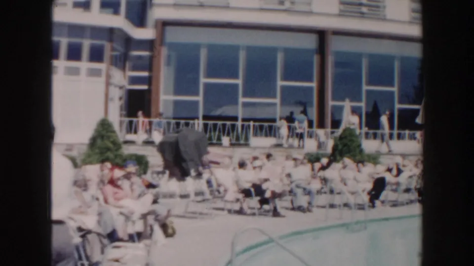1960 Miami resort pool scene with adults gathered on lounge chairs beside turquoise water and a large windowed building.
