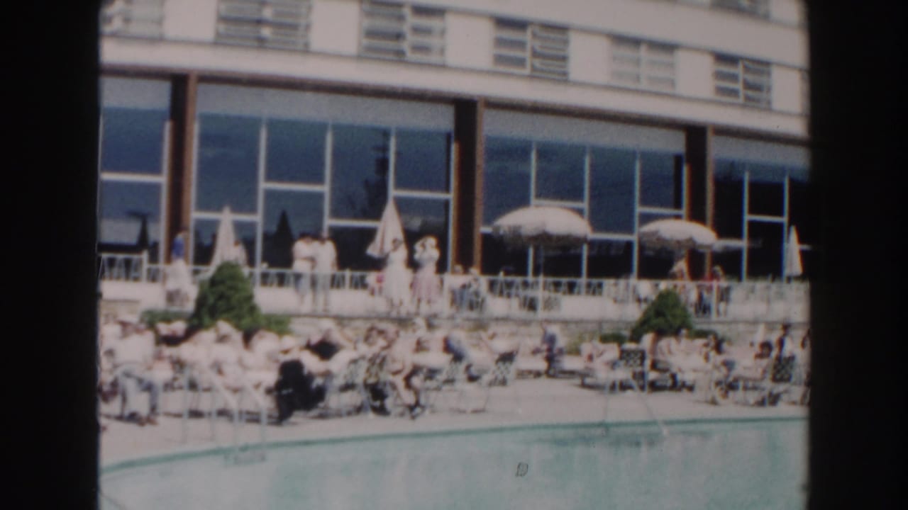 Crowded hotel poolside with lounge chairs, umbrellas, and guests near a modern building.