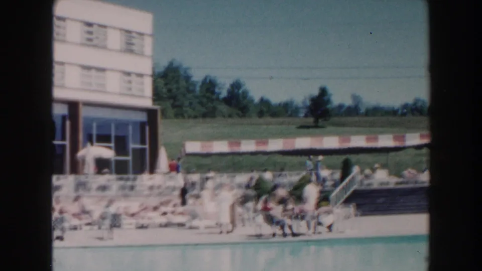 1960 Miami hotel poolside showing guests near the water, patio umbrellas, stairs, and a grassy area beyond.