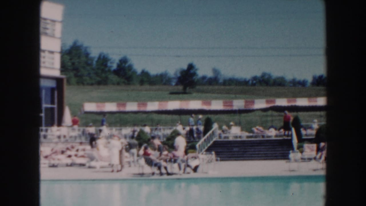 1960 Miami poolside scene with visitors relaxing near lounge chairs, steps, a striped awning, and grassy grounds beyond.