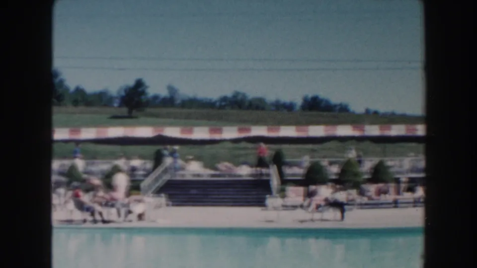 Miami poolside footage from 1960 showing people sitting and strolling near loungers, steps, and a red-and-white striped awning.