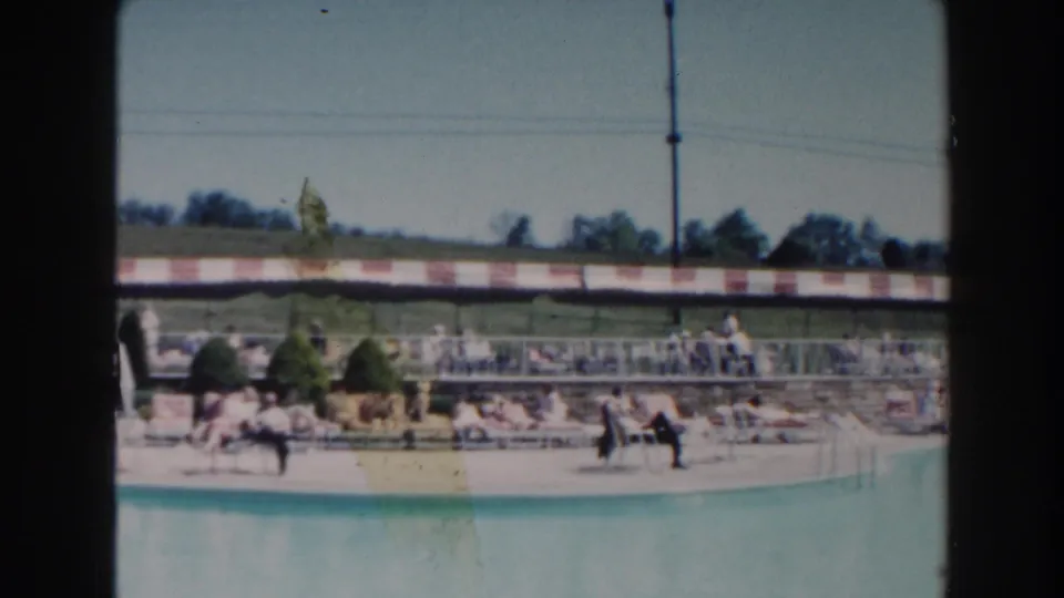 Miami poolside scene from 1960 with people near loungers, striped shade, pool ladder, deck furniture, and grassy grounds behind.