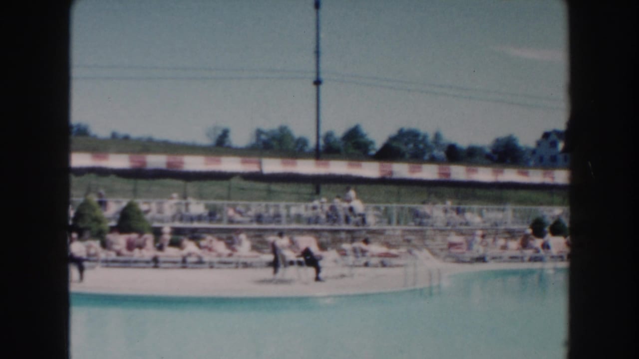 Outdoor swimming pool with lounge chairs, distant visitors, barrier, trees, and utility poles.