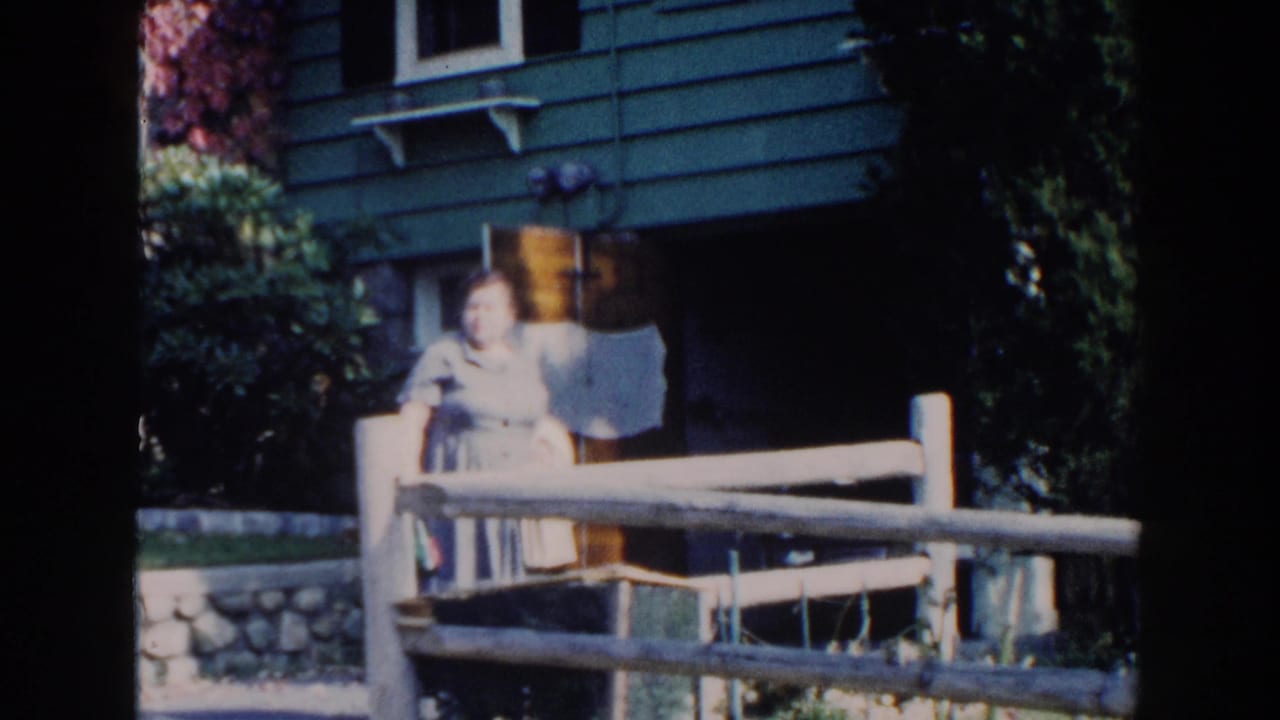 Woman faces the camera from behind a wooden fence outside a house.