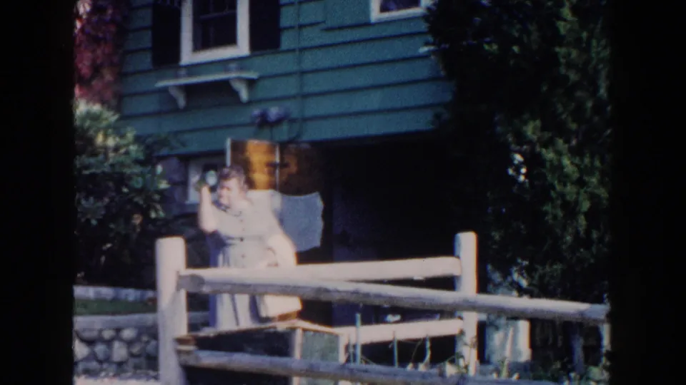 In the final frame, the woman raises a small light object toward the camera while standing outside the Miami house.