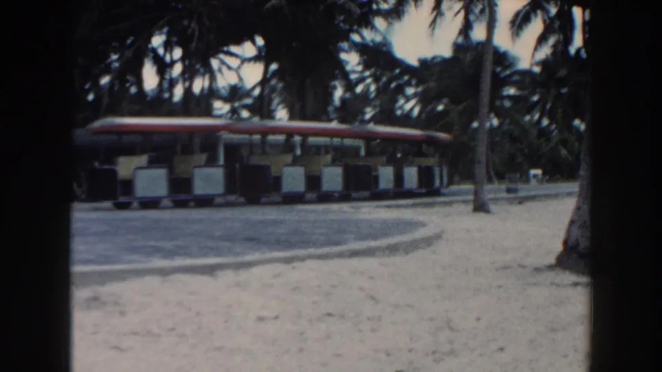 The red-roof resort tram appears farther along the paved path, framed by palms and sandy ground in Miami archival footage.