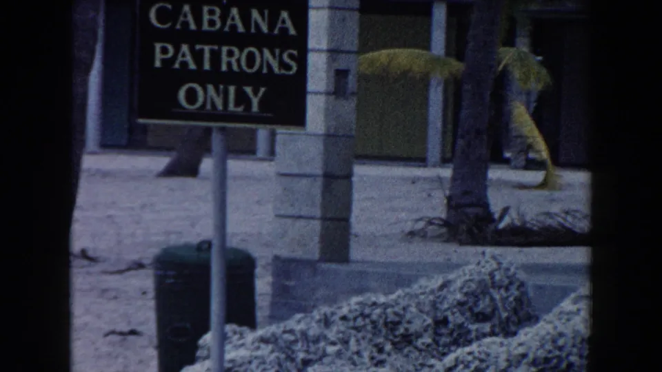 A CABANA PATRONS ONLY sign stands near palm trees and cabana structures in the 1960 Miami resort scene.