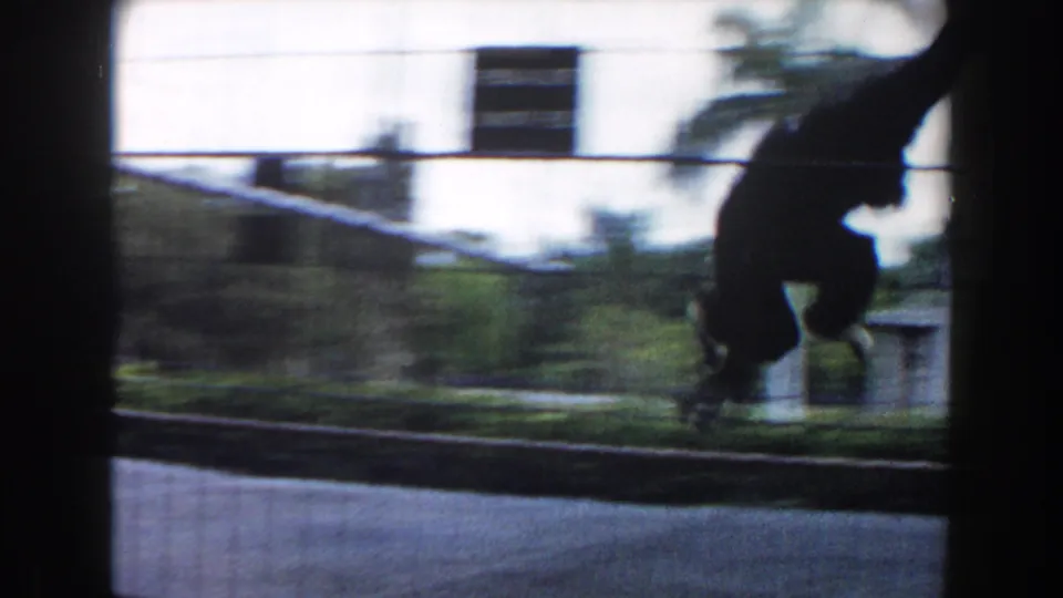 A monkey swings across the cage in 1960 Miami zoo footage, silhouetted against bright outdoor structures and pavement.