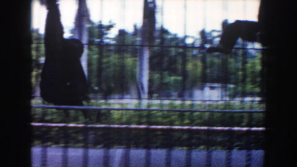 1960 Miami home-movie frame of a primate hanging or climbing inside a barred zoo enclosure, filmed through dark cage lines.