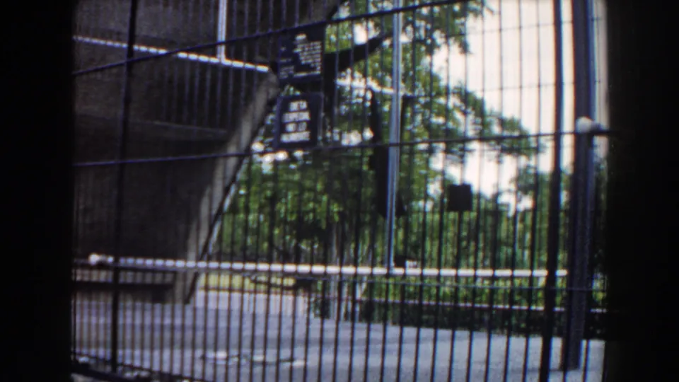 A visitor-shot view through a zoo enclosure with bars, posted signs, pavement, and trees in the supplied 1960 Miami footage.