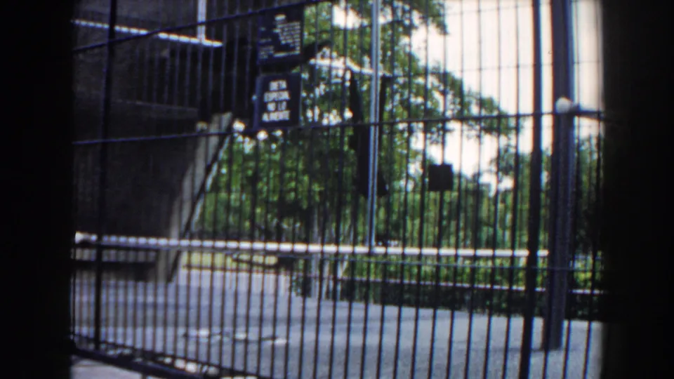 Metal cage fencing, small warning signs, and trees seen through the enclosure in supplied 1960 Miami 8mm footage.