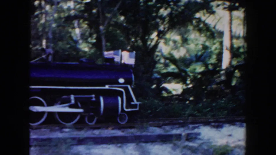 A small dark miniature locomotive moves through a wooded park setting, likely part of the same 1960 Miami outing.