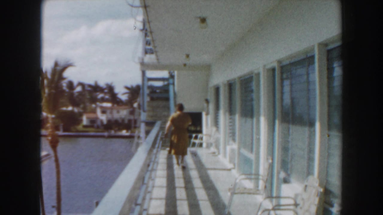 Woman walking along a balcony beside a canal and palm trees.