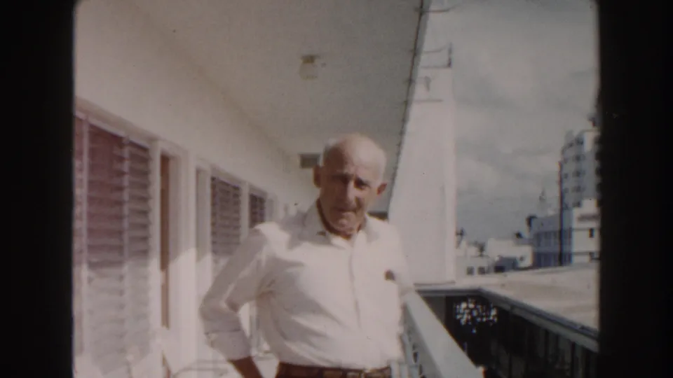 Near the end of the 1960 Miami clip, the older man turns slightly toward the camera on the outdoor hotel corridor.
