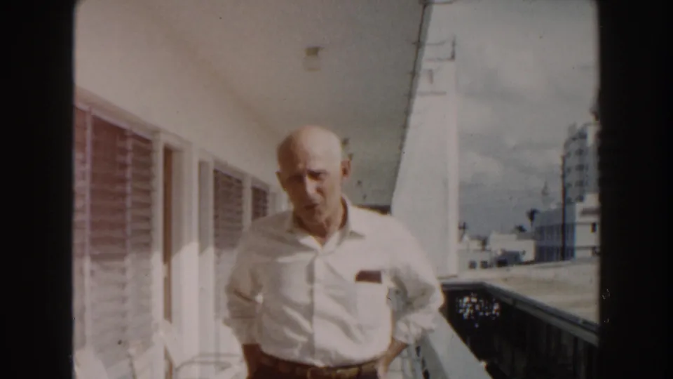 The 1960 Miami balcony view shows the elderly man closer to center, with a railing, hotel facade, and urban buildings behind him.