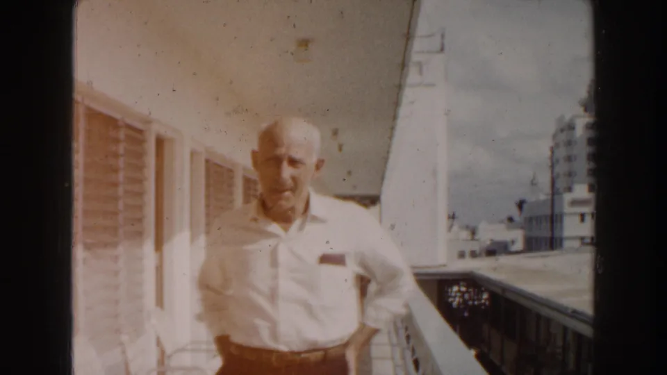 The final 1960 Miami frame shows the elderly man facing the camera on the balcony, with warm film fading, railing, windows, and city buildings visible.