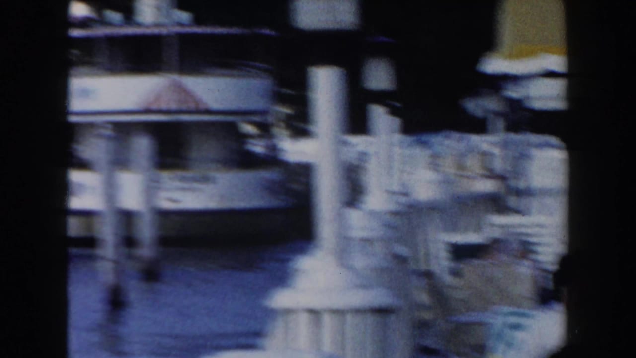 Blurred dockside view with a boat, posts, and stacked chairs near the water.
