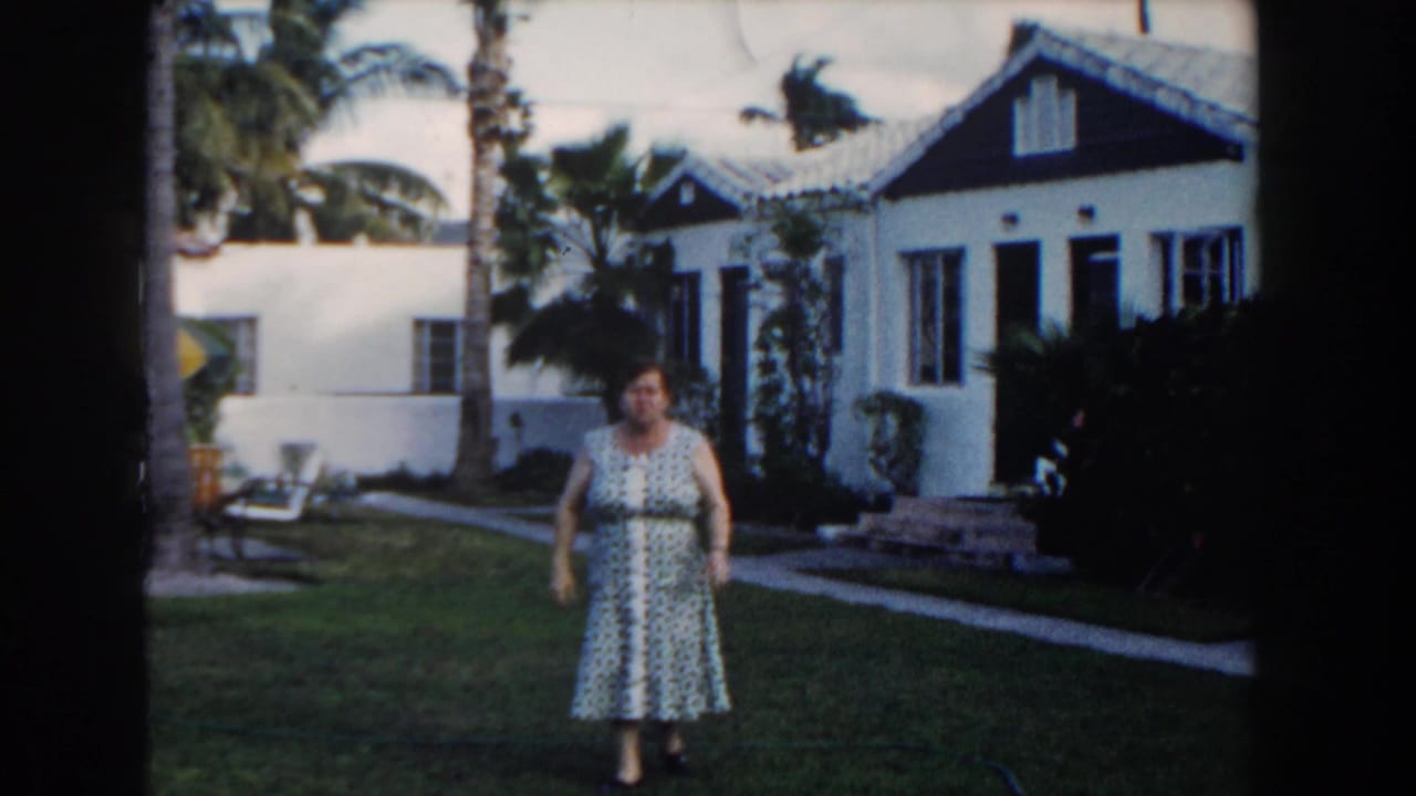 Woman in a patterned dress standing on a lawn outside a white house.