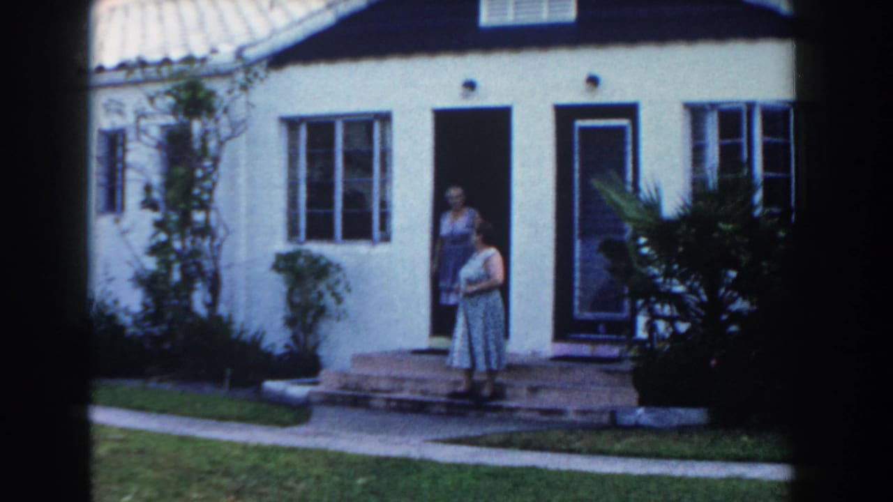Two women stand near the front steps of a white stucco house.