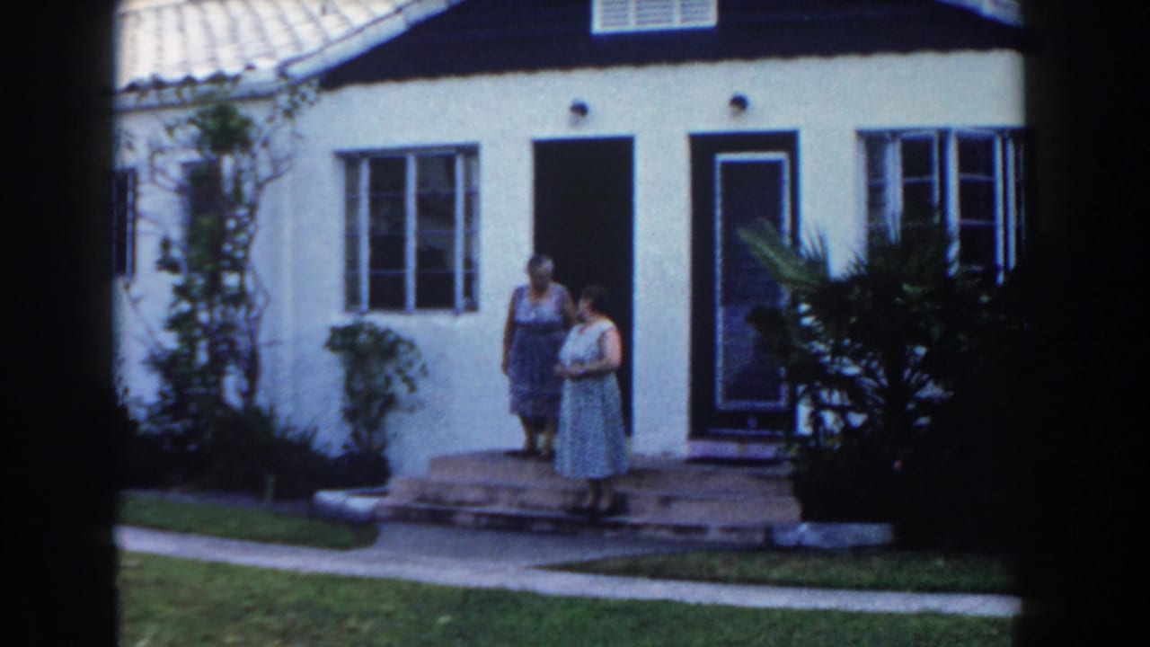 Two women stand outside a house, one on the steps and one near the doorway.