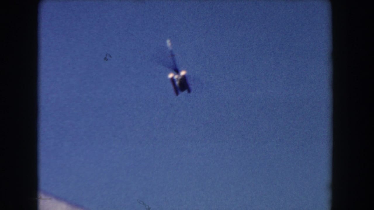 1960 Miami 8mm frame showing a distant blurry aircraft or helicopter against a blue sky.