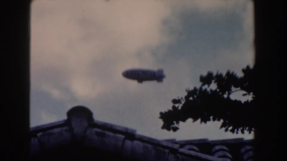 1960 Miami 8mm view of the Goodyear blimp moving across the sky over a tiled residential roof.