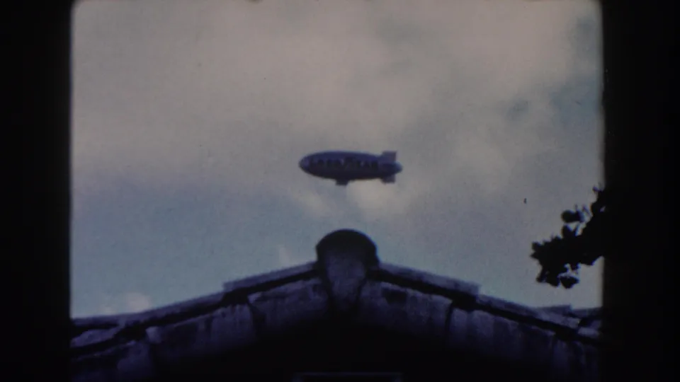 1960 Miami home-movie view of a Goodyear blimp above a roof peak, with soft focus and faded sky color.
