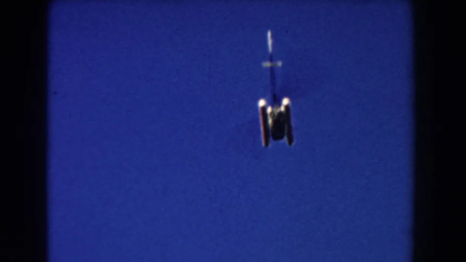 Low-angle 8mm frame of a helicopter centered in a deep blue Miami sky, with landing gear visible.