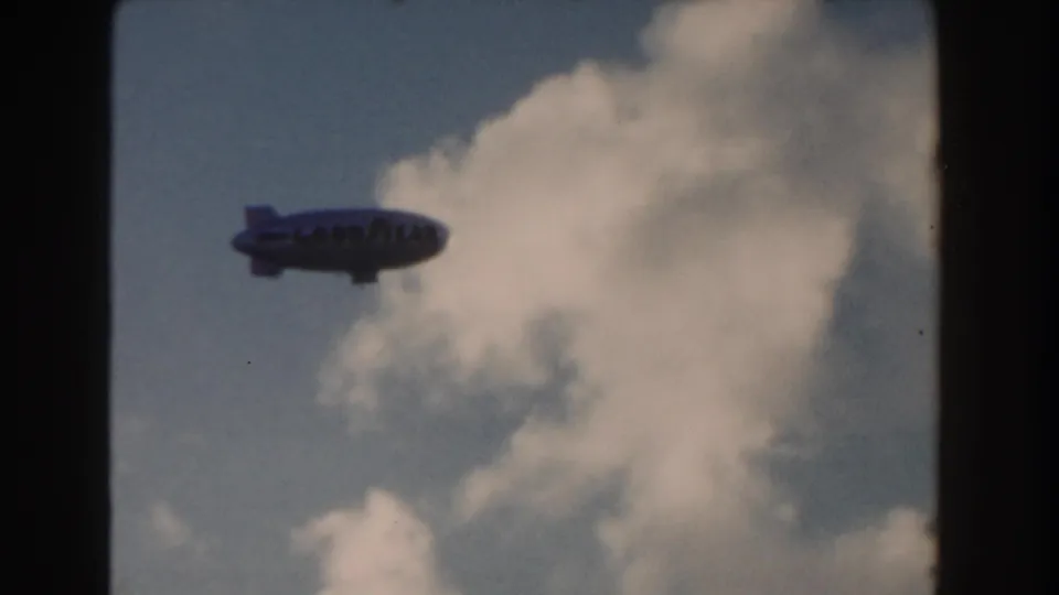 1960 Miami 8mm frame with the Goodyear blimp passing in front of a bright cloud bank.