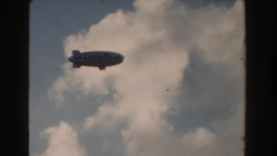 1960 Miami 8mm frame showing the Goodyear blimp crossing below a large sunlit cloud.