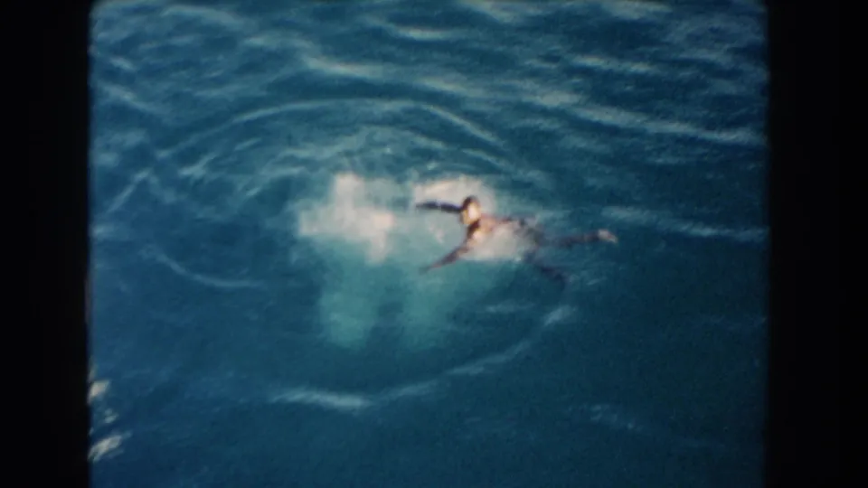 1960 Miami home-movie frame showing a swimmer moving through bright turquoise ocean water with visible film borders.
